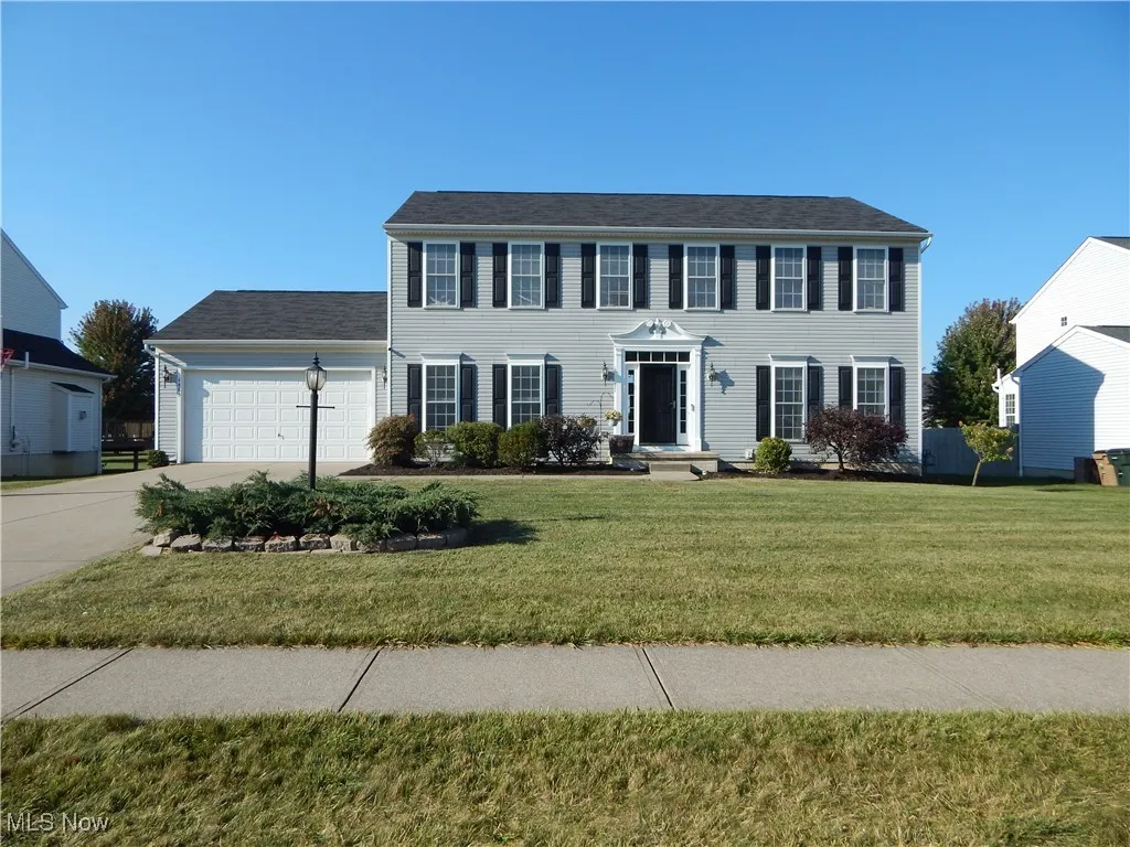 Colonial-style house featuring a garage, concrete driveway, and a front yard