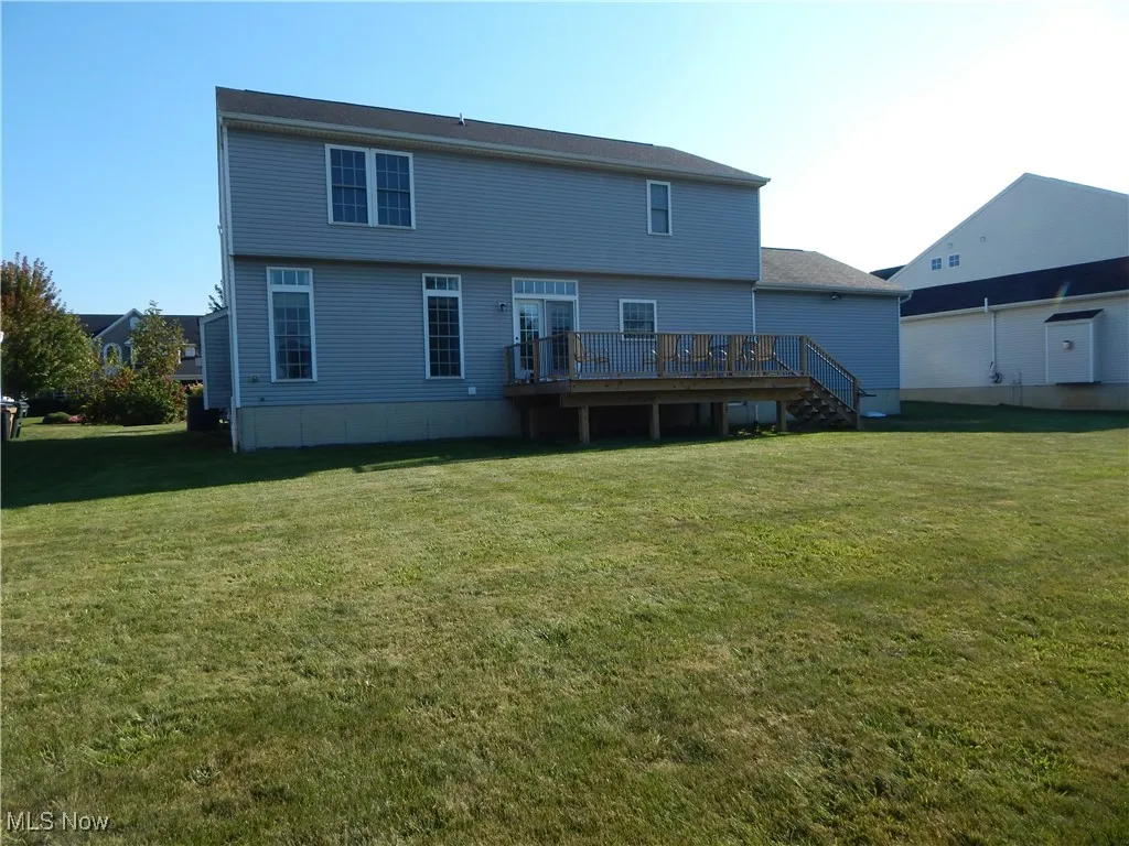 Rear view of property featuring a deck, a lawn, and stairway