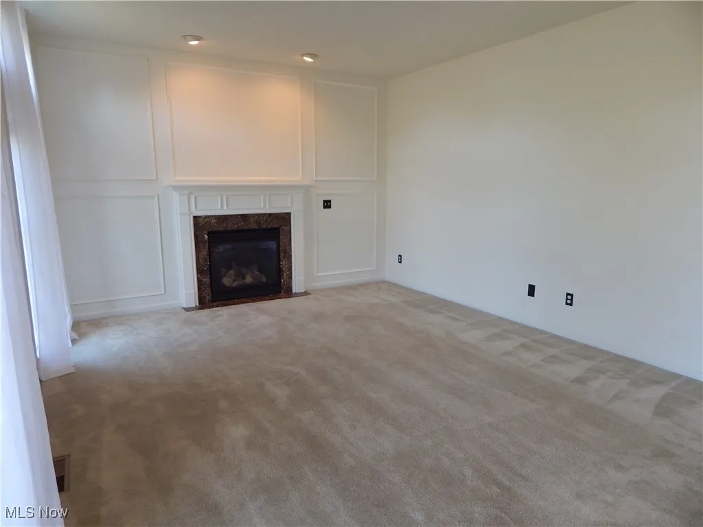 Unfurnished living room featuring light carpet, a fireplace, and a decorative wall