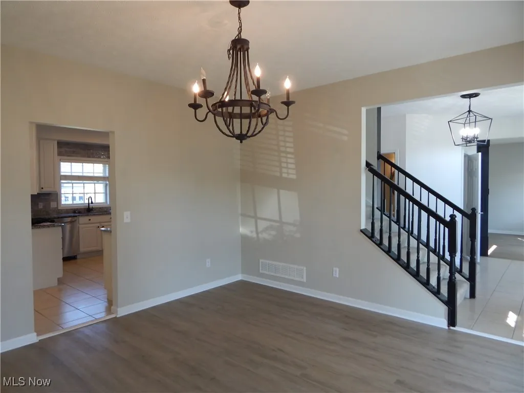 Unfurnished dining area with a chandelier, light wood-style flooring, and stairs