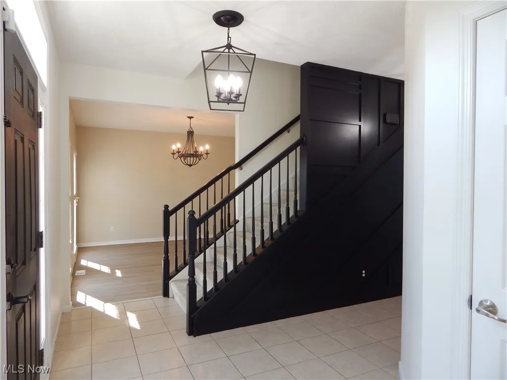 Foyer with a chandelier, light tile patterned floors, and stairs