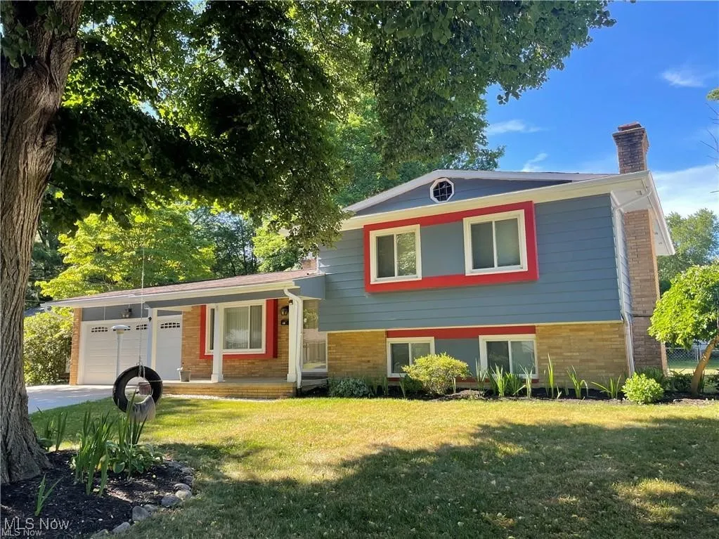 Tri-level home featuring a porch, a chimney, an attached garage, a front yard, and brick siding