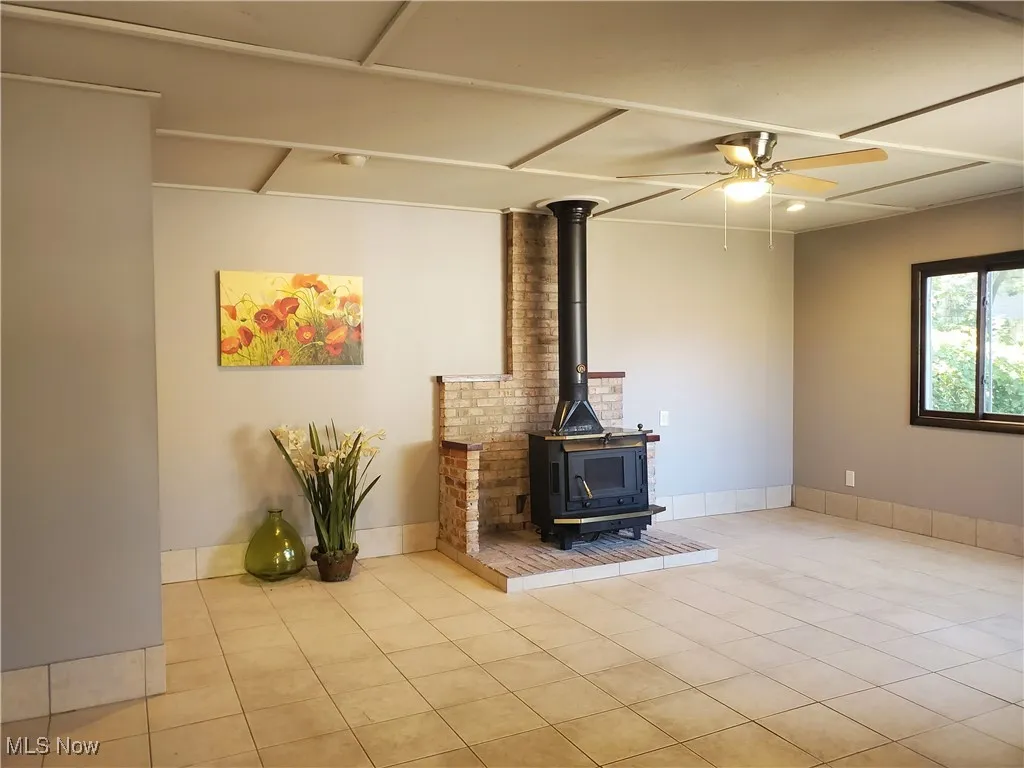 Unfurnished living room with a wood stove, tile patterned floors, and a ceiling fan