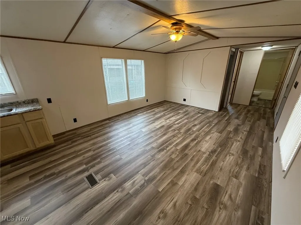 Unfurnished bedroom featuring dark wood-type flooring, vaulted ceiling, and a ceiling fan