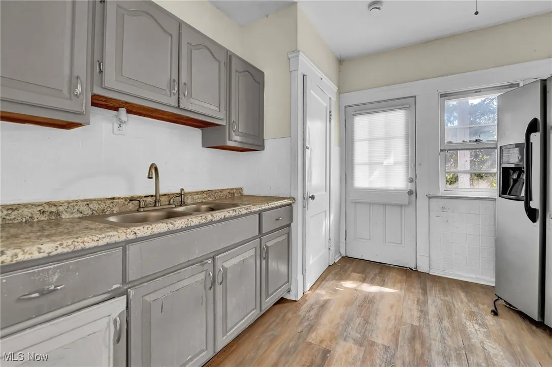 Kitchen with gray cabinets, light wood-type flooring, stainless steel fridge with ice dispenser, and light stone countertops