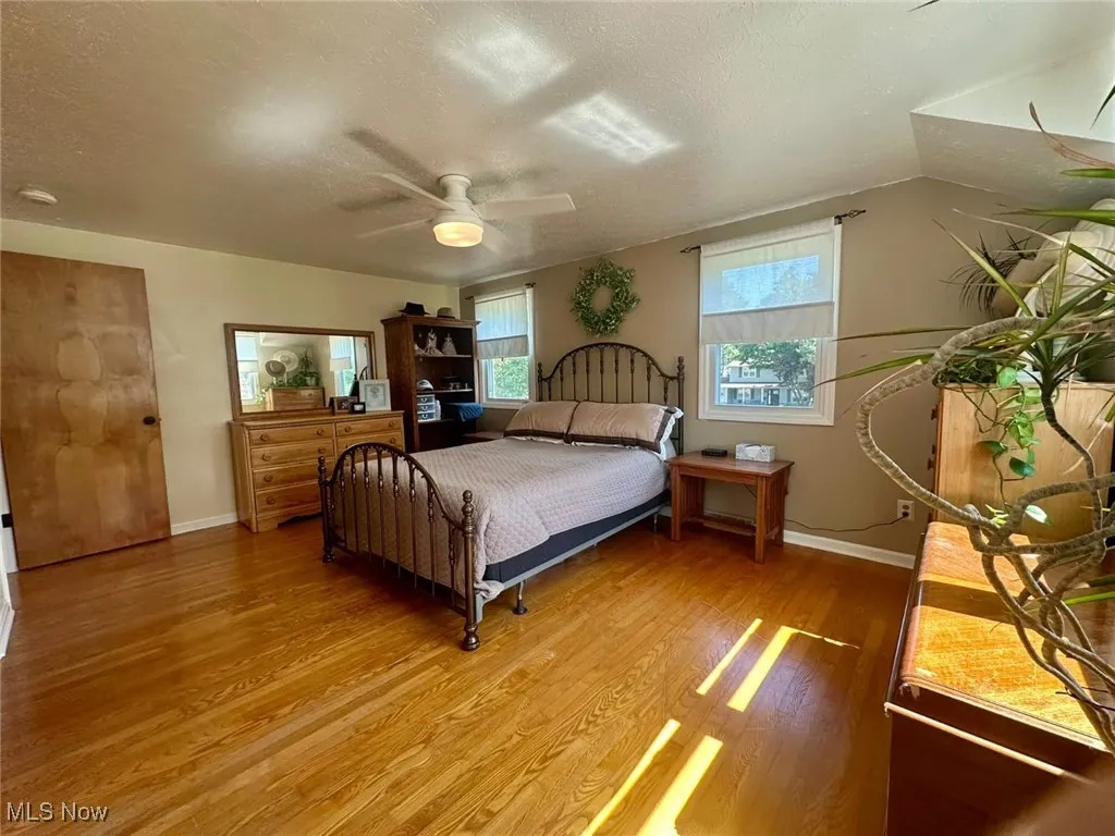 Bedroom with a textured ceiling, multiple windows, light wood finished floors, and ceiling fan
