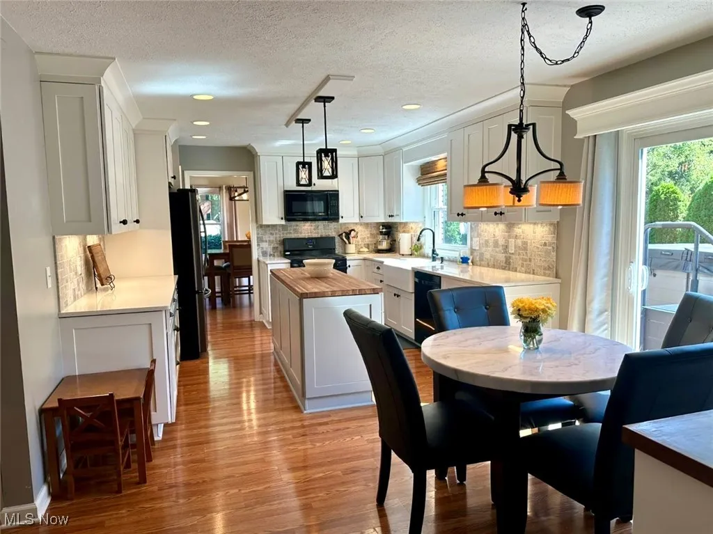 Kitchen with butcher block counters, backsplash, black appliances, light wood-style flooring, and decorative light fixtures