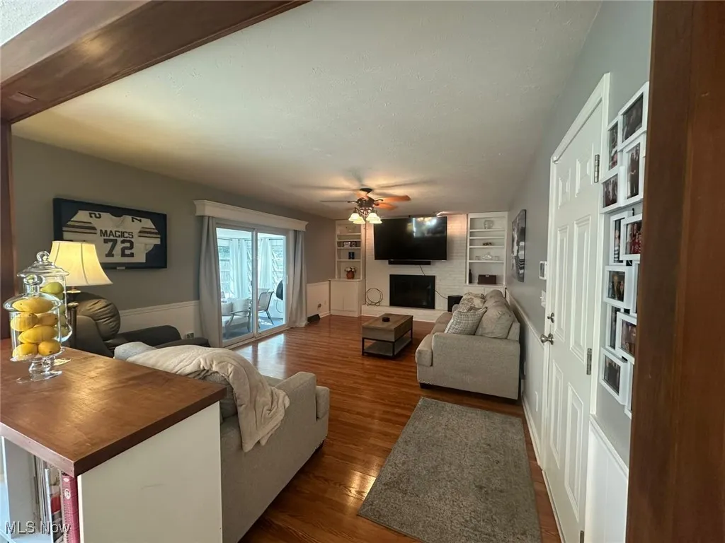 Living area with built in features, wood finished floors, a brick fireplace, a textured ceiling, and a ceiling fan