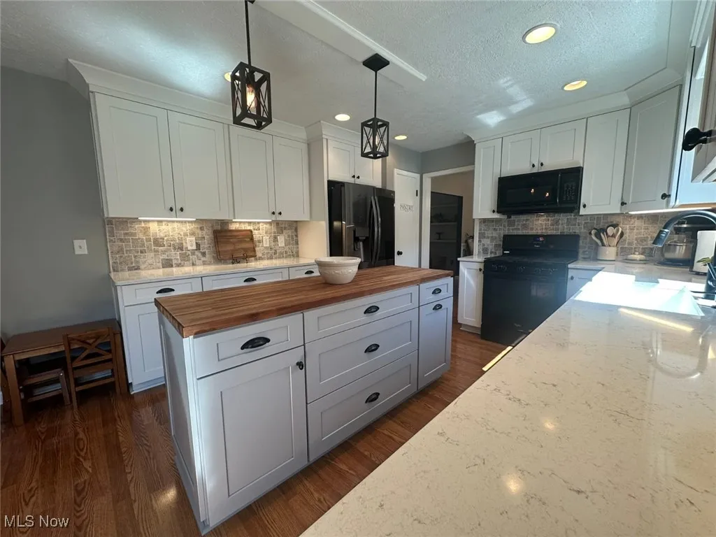 Kitchen with wood counters, white cabinetry, pendant lighting, black appliances, and a textured ceiling