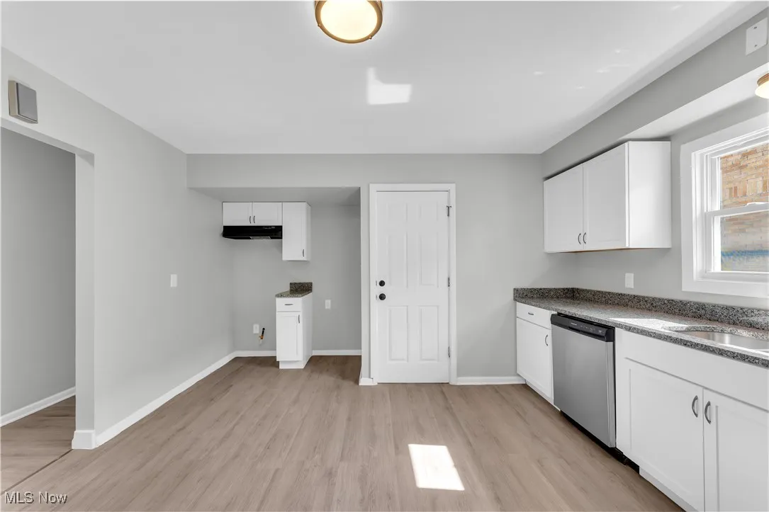 Kitchen featuring white cabinetry, light wood-type flooring, stainless steel dishwasher, and dark stone counters