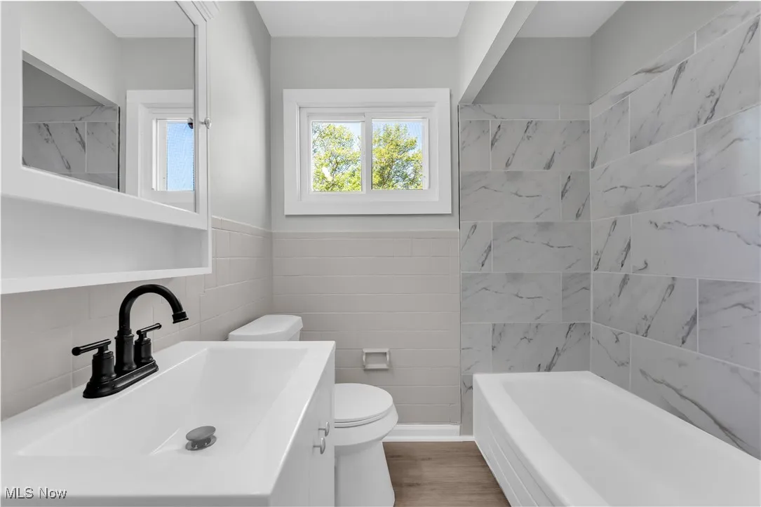 Full bath featuring vanity, tile walls, shower / bath combination, light wood-style floors, and a wainscoted wall