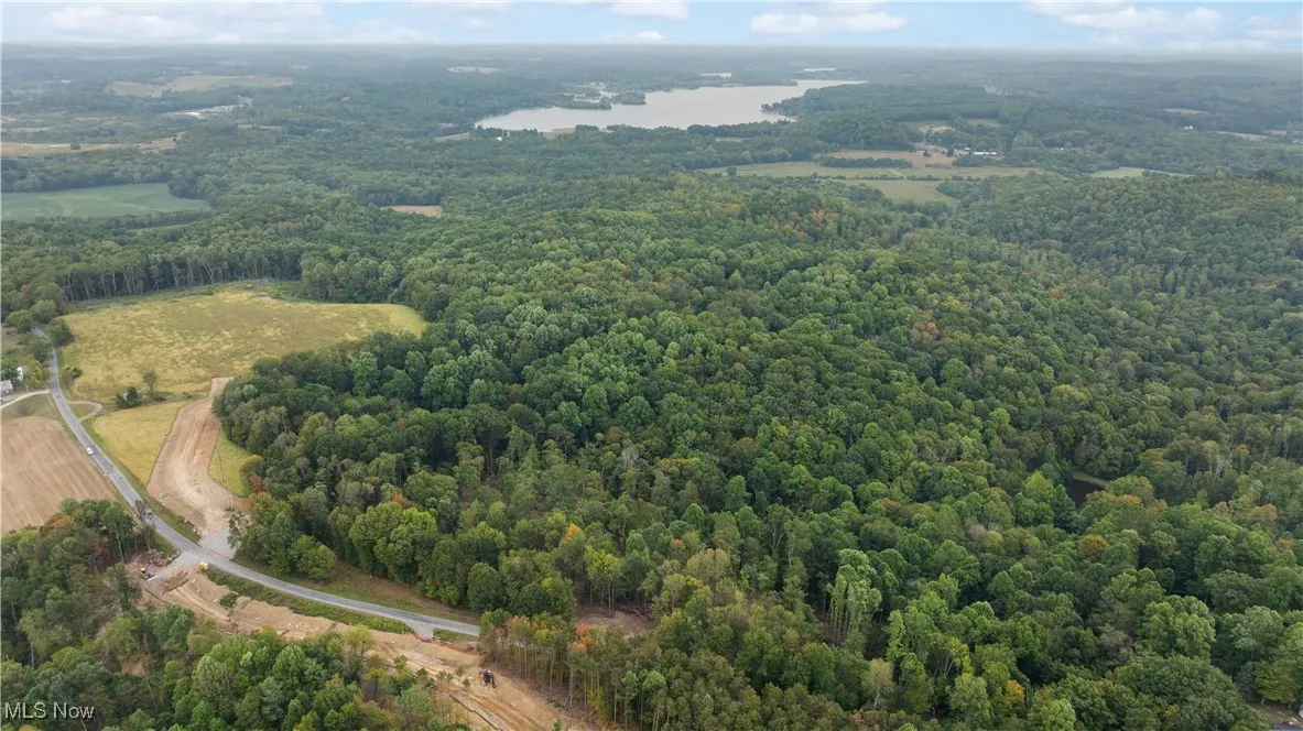 Aerial view of property and surrounding area with a nearby body of water and a heavily wooded area