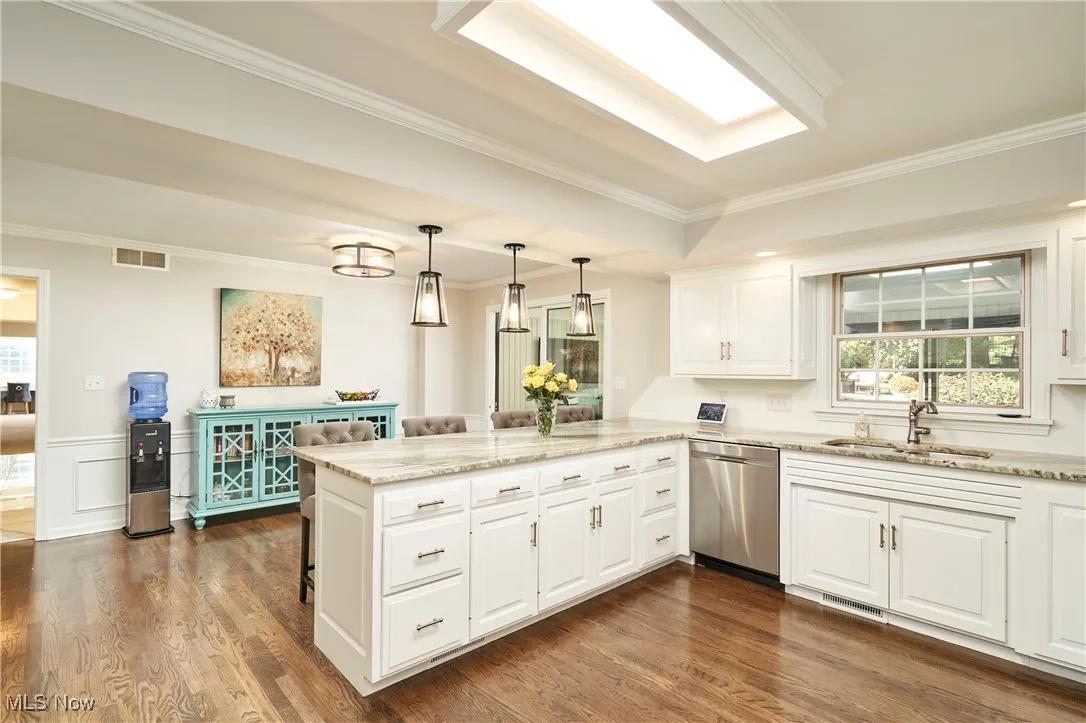 Kitchen featuring healthy amount of natural light, ornamental molding, a breakfast bar, a peninsula, and light stone counters