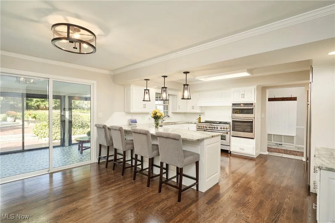Kitchen featuring white cabinetry, crown molding, dark wood-style floors, pendant lighting, and a kitchen bar
