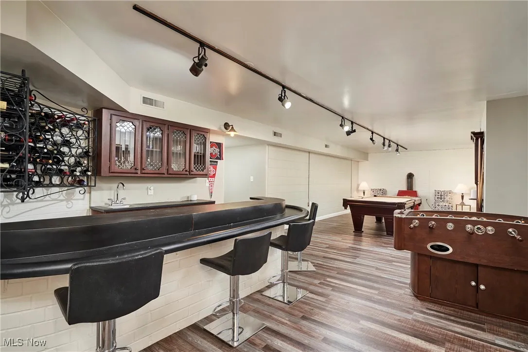 Indoor wet bar with track lighting, glass insert cabinets, light wood-type flooring, and dark countertops