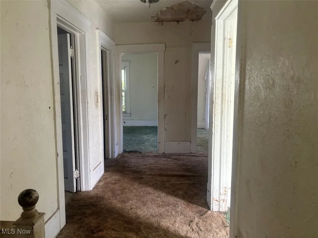 Corridor featuring a textured wall and dark colored carpet