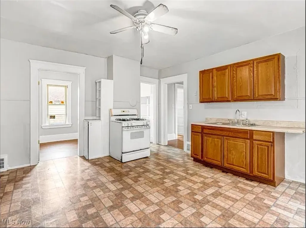 Kitchen with white range with gas stovetop, light countertops, brown cabinetry, and brick patterned flooring