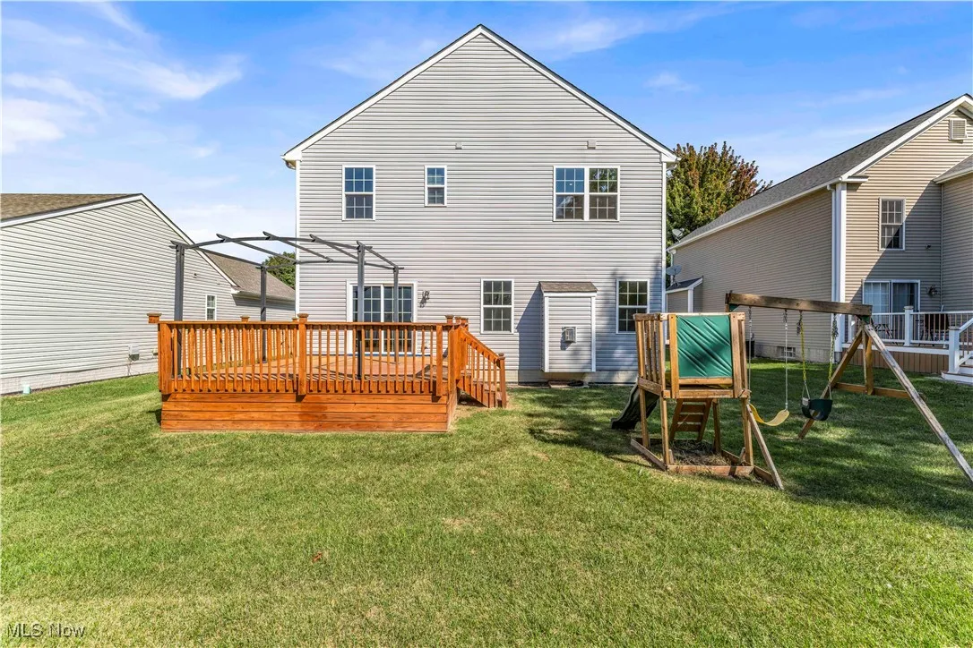 Back of property with a playground, a lawn, and a deck