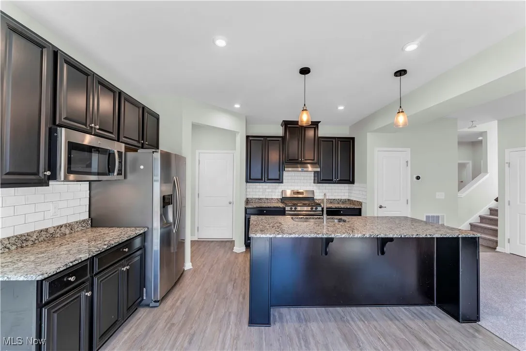 Kitchen featuring a breakfast bar area, decorative light fixtures, light stone counters, dark brown cabinets, and appliances with stainless steel finishes