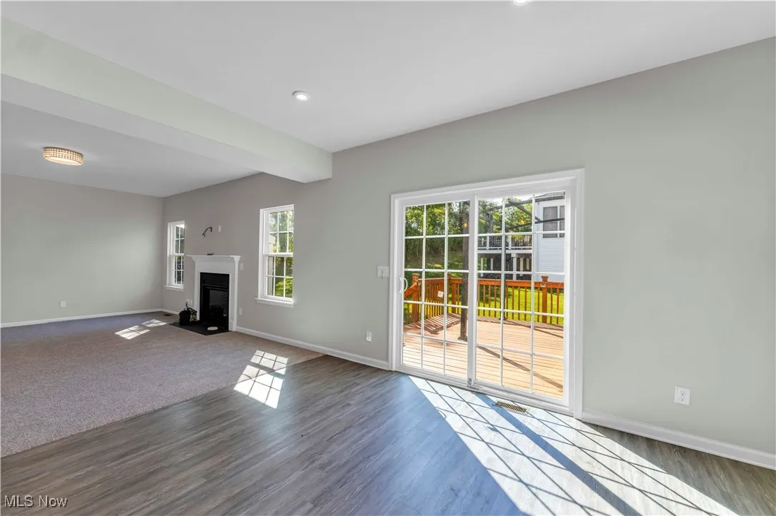 Unfurnished living room with a fireplace with flush hearth, wood finished floors, beam ceiling, and recessed lighting