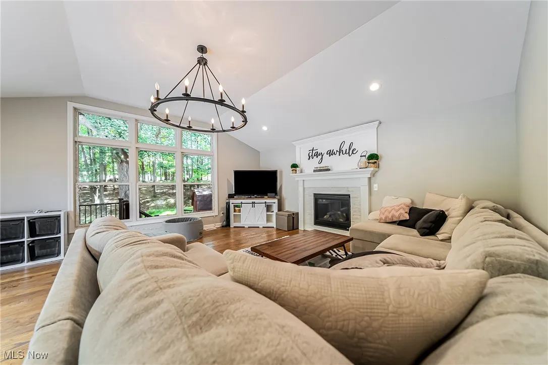 Living room with lofted ceiling, a tile fireplace, light wood-style flooring, a chandelier, and recessed lighting