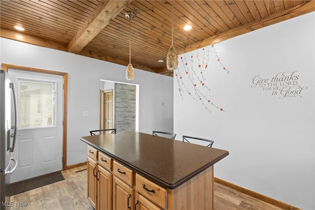 Kitchen with a center island, hanging light fixtures, stainless steel refrigerator with ice dispenser, a wood ceiling with exposed beams, and light wood-type flooring