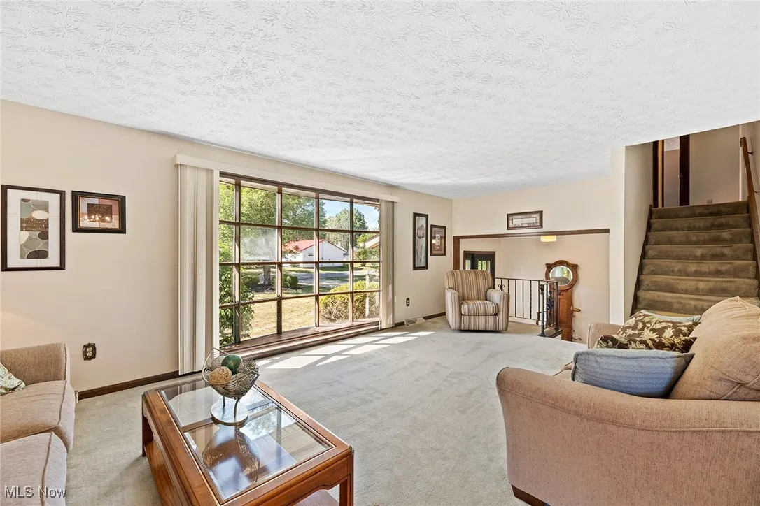 Living area with carpet flooring, stairway, and a textured ceiling