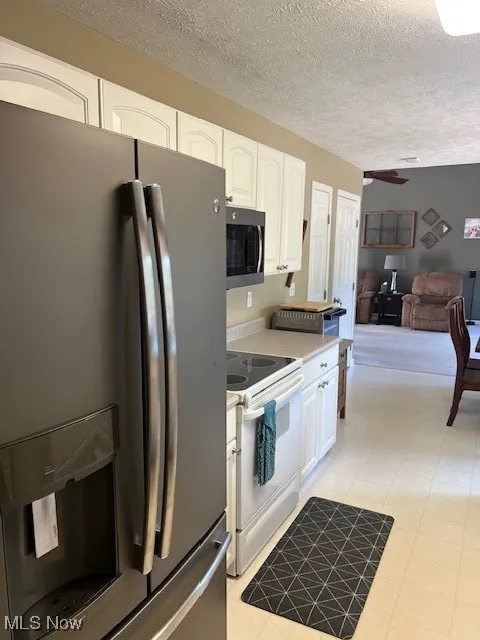 Kitchen featuring appliances with stainless steel finishes, a textured ceiling, light countertops, white cabinetry, and light floors