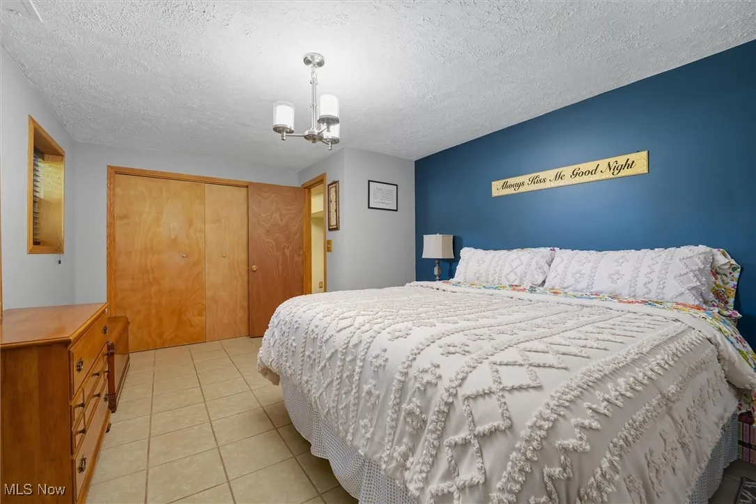 Bedroom featuring a closet, light tile patterned floors, a textured ceiling, and a chandelier
