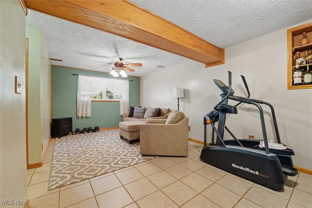 Exercise area featuring ceiling fan, light tile patterned floors, and a textured ceiling