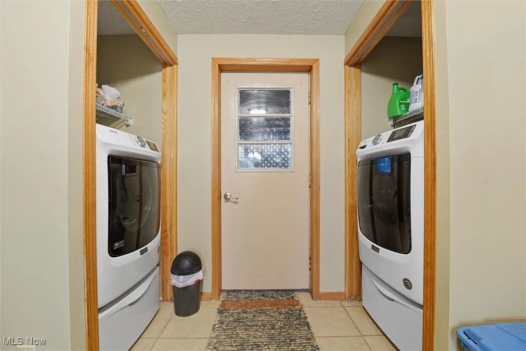 Laundry area with light tile patterned flooring, washer and clothes dryer, and a textured ceiling