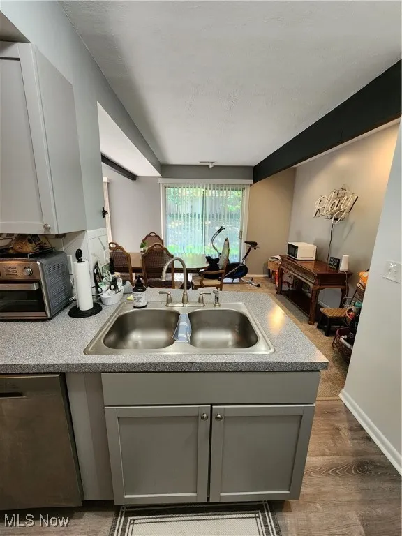 Kitchen with gray cabinetry, dishwashing machine, light countertops, a peninsula, and light wood finished floors