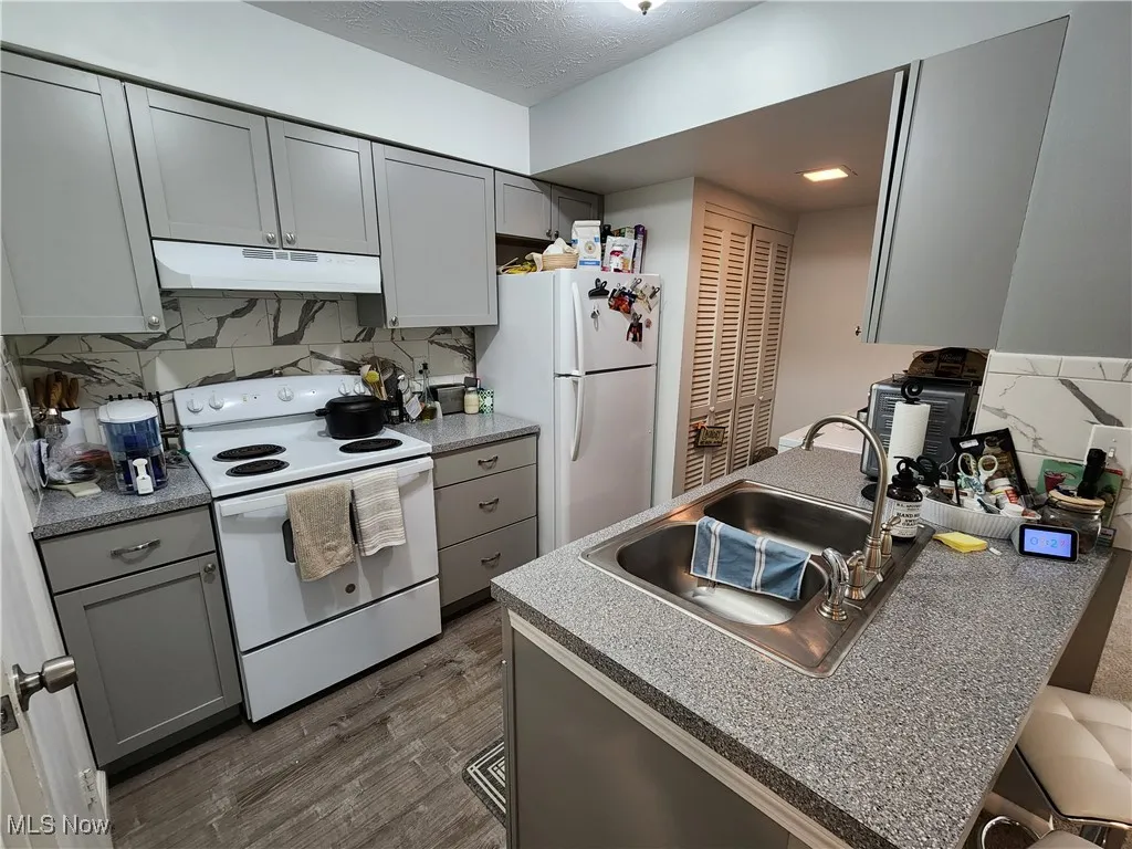 Kitchen with gray cabinetry, white appliances, tasteful backsplash, under cabinet range hood, and a textured ceiling