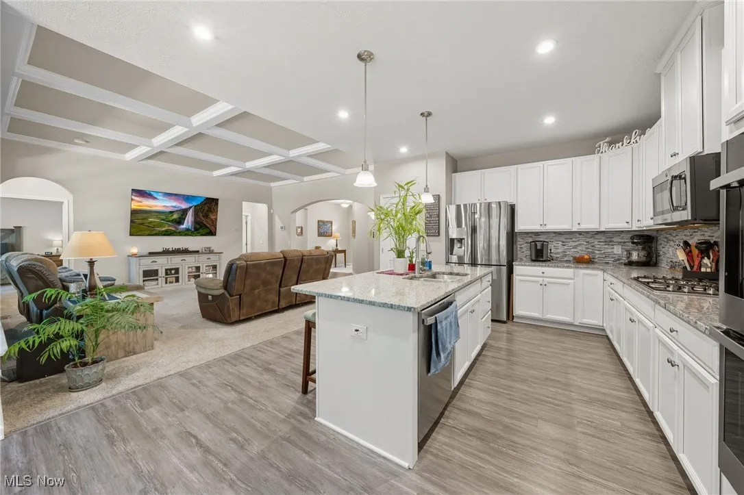 Kitchen featuring coffered ceiling, arched walkways, a breakfast bar area, beam ceiling, and white cabinetry