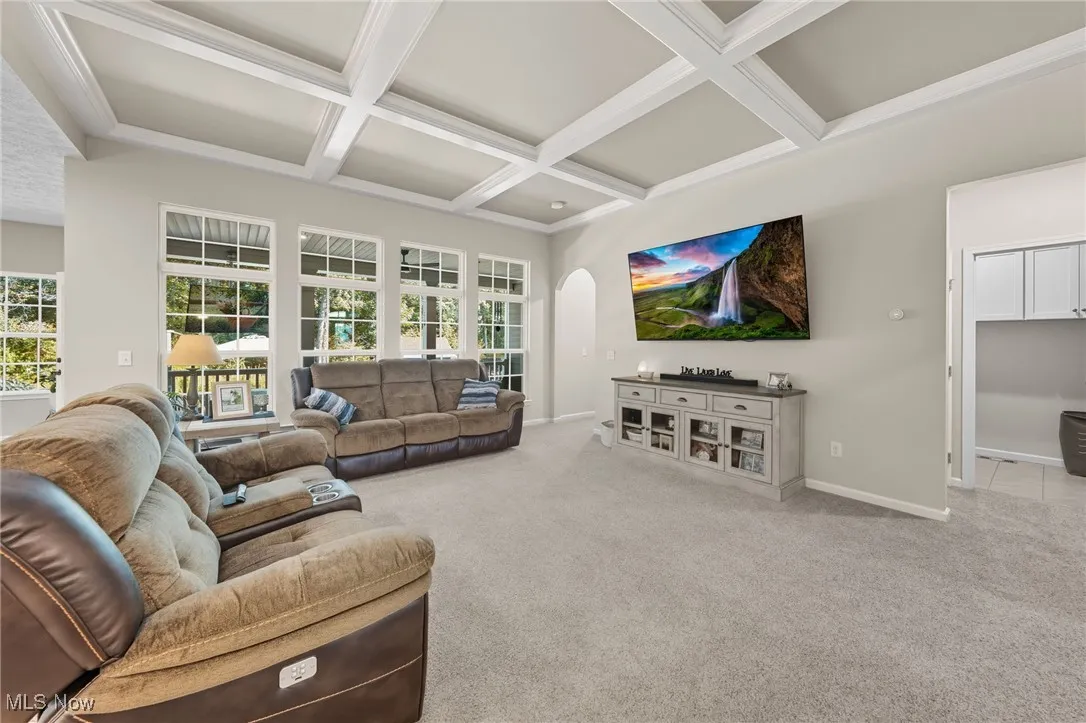 Living room featuring beamed ceiling, coffered ceiling, light colored carpet, and arched walkways