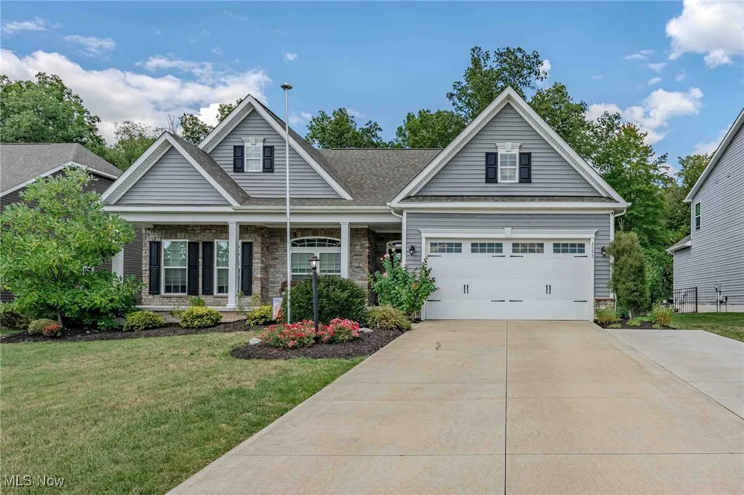 View of front facade with covered porch, a garage, driveway, stone siding, and a front yard