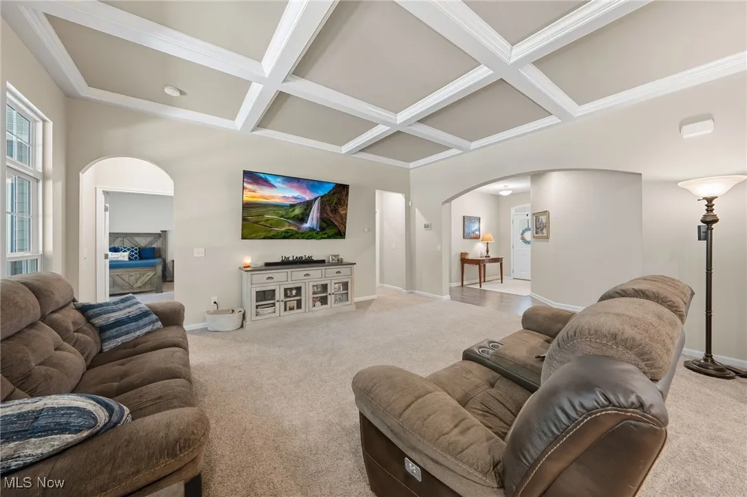 Living area with arched walkways, coffered ceiling, beam ceiling, and carpet flooring