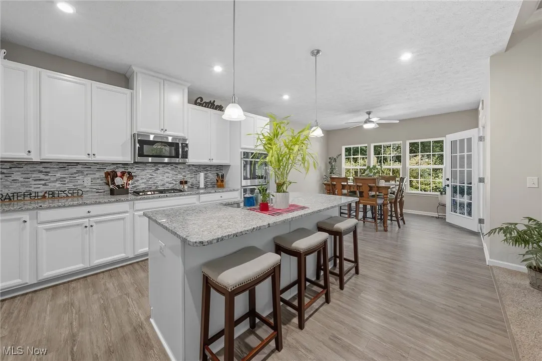 Kitchen featuring hanging light fixtures, decorative backsplash, a center island, a kitchen breakfast bar, and light wood finished floors