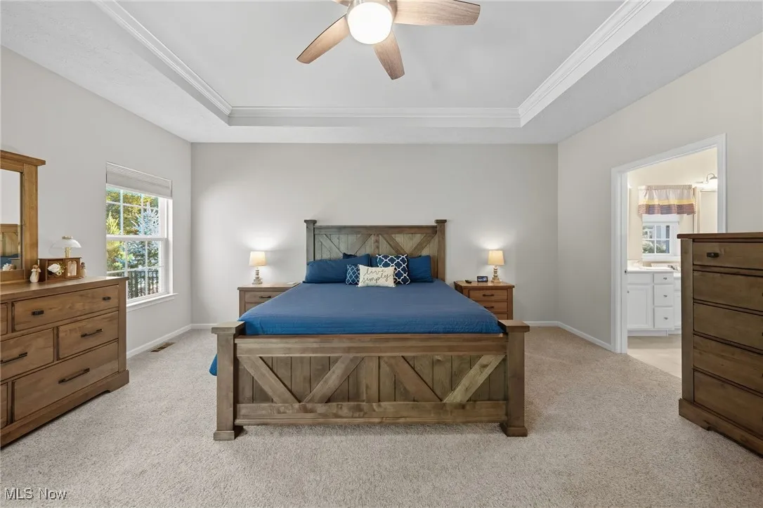 Bedroom featuring light carpet, a raised ceiling, a ceiling fan, ornamental molding, and ensuite bath