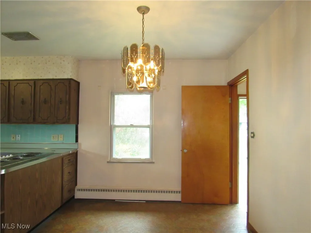 Kitchen featuring decorative backsplash, a baseboard heating unit, a chandelier, light countertops, and pendant lighting