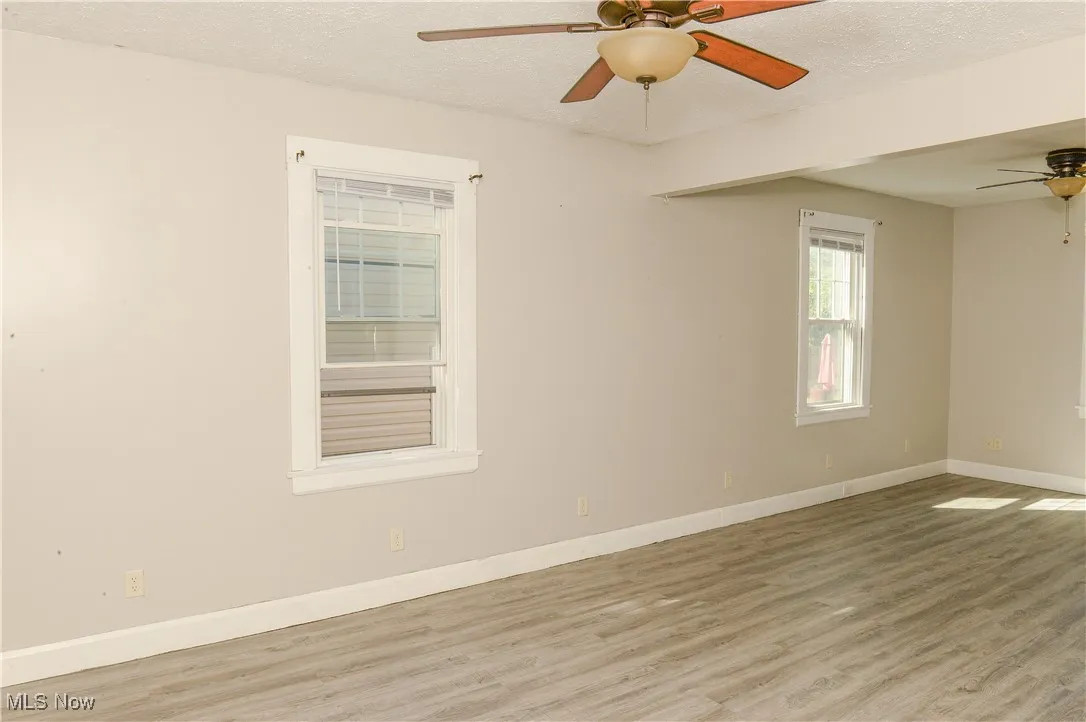 Empty room with a textured ceiling, wood finished floors, and a ceiling fan