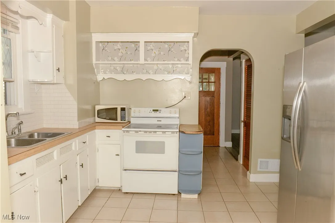 Kitchen with tasteful backsplash, white appliances, arched walkways, white cabinetry, and light​​‌​​​​‌​​‌‌​‌‌​​​‌‌​‌​‌​‌​​​‌​​ countertops