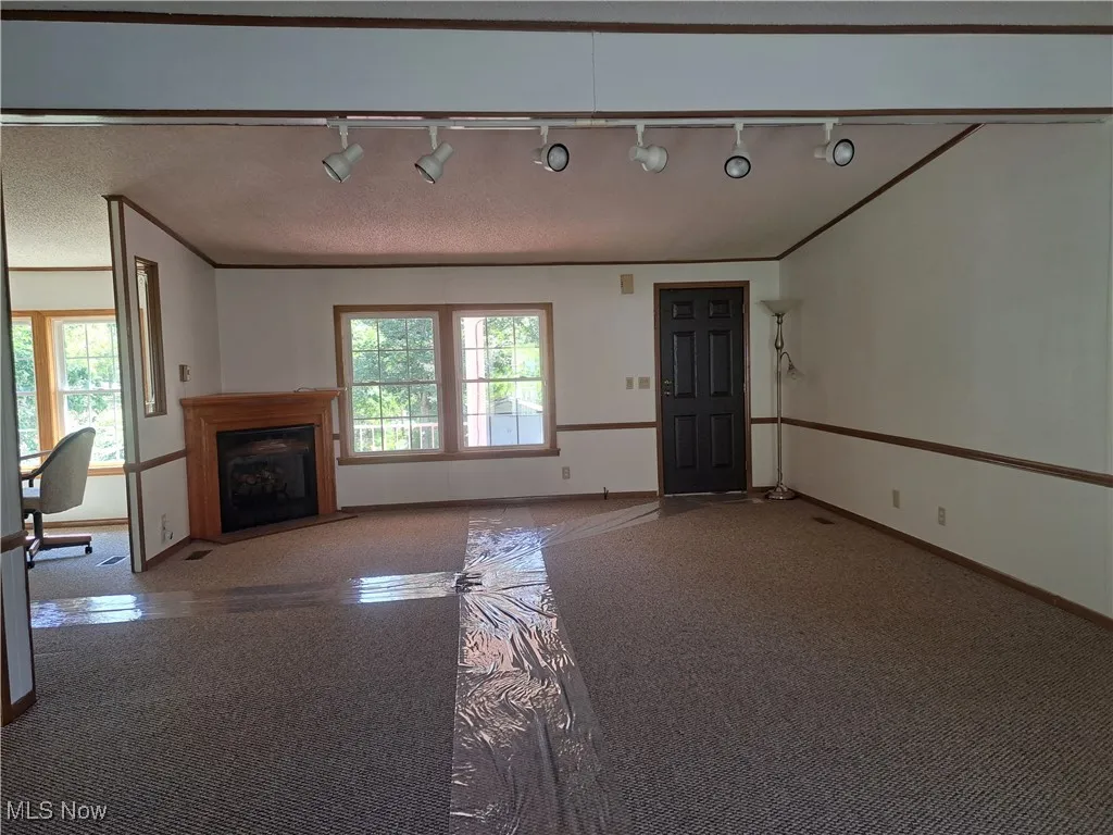 Unfurnished living room featuring carpet, track lighting, a fireplace with flush hearth, ornamental molding, and a textured ceiling