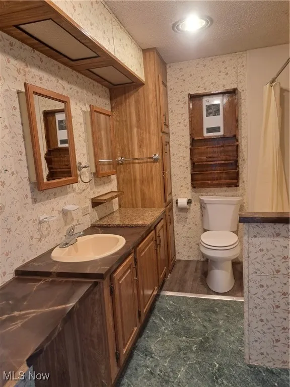 Full bath featuring vanity, a textured ceiling, wallpapered walls, and a shower with shower curtain