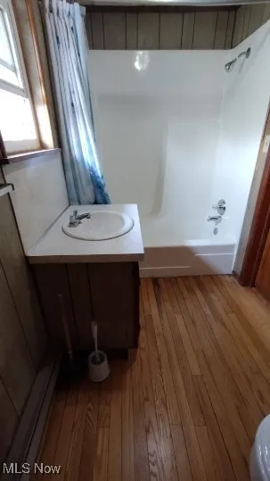 Full bathroom featuring shower / tub combo, vanity, light wood-style flooring, and a baseboard heating unit