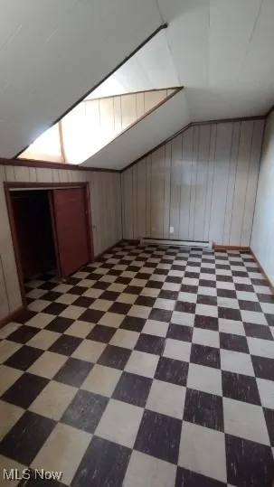 Additional living space featuring vaulted ceiling, wood walls, a baseboard heating unit, and dark flooring