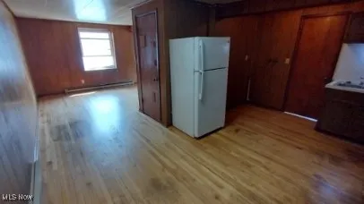 Kitchen featuring wooden walls, light wood finished floors, freestanding refrigerator, and baseboard heating