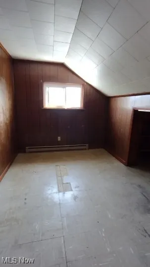 Additional living space with wooden walls, light flooring, vaulted ceiling, and a baseboard heating unit