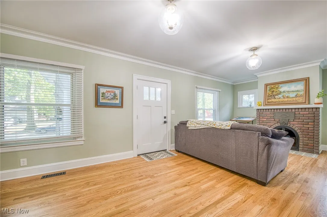 Living room with crown molding, a brick fireplace, and light wood-style floors