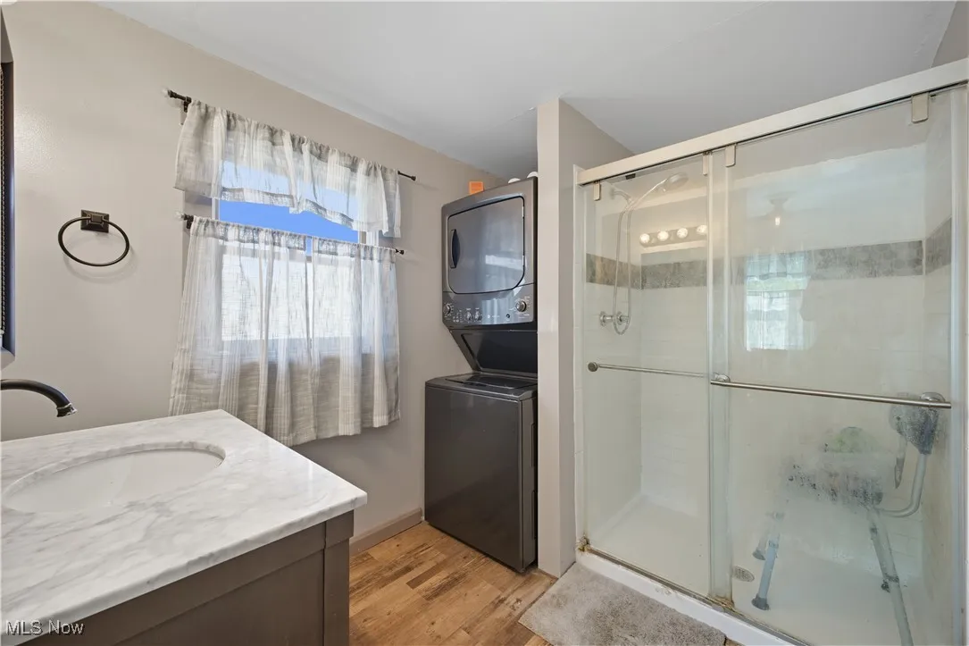 Full bathroom with vanity, light wood finished floors, a stall shower, and stacked washing machine and dryer